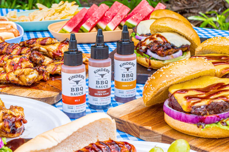 A selection of barbecue foods on a table with three bottles of BBQ sauce