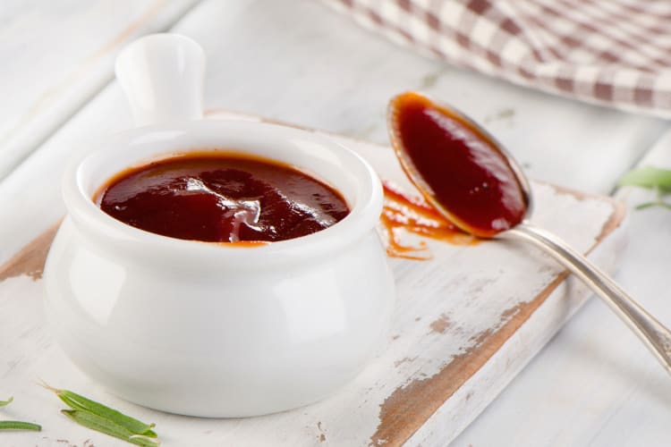 A jar of sweet BBQ sauce with a spoon next to it