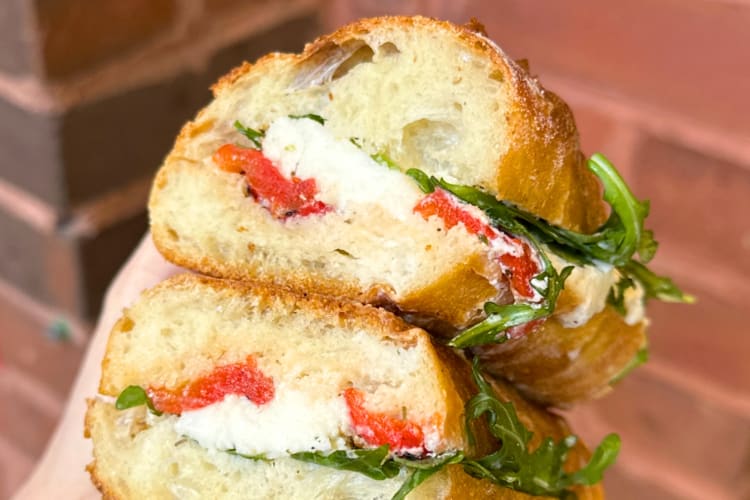A baguette sandwich with mozzarella, red peppers and arugula