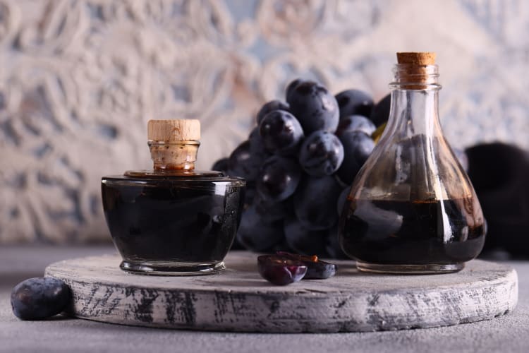 Glass containers of balsamic vinegar next to grapes