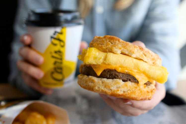 A person holding a biscuit breakfast sandwich and a cup of coffee