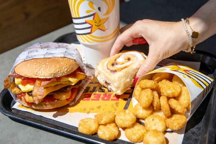 A breakfast burger, cinnamon roll and hash brown on a tray