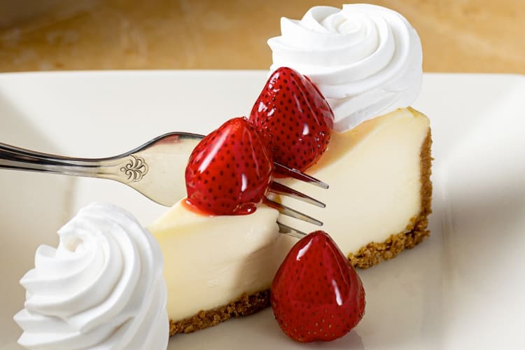 A person cutting a piece of plain cheesecake with strawberries