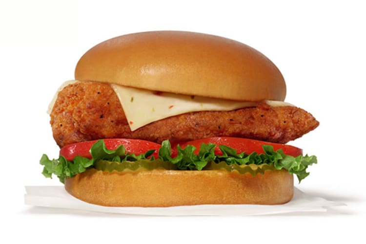 A spicy chicken sandwich with cheese, pickles and tomatoes