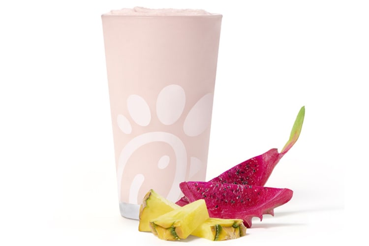 A fruit smoothie next to fresh dragonfruit and pineapple