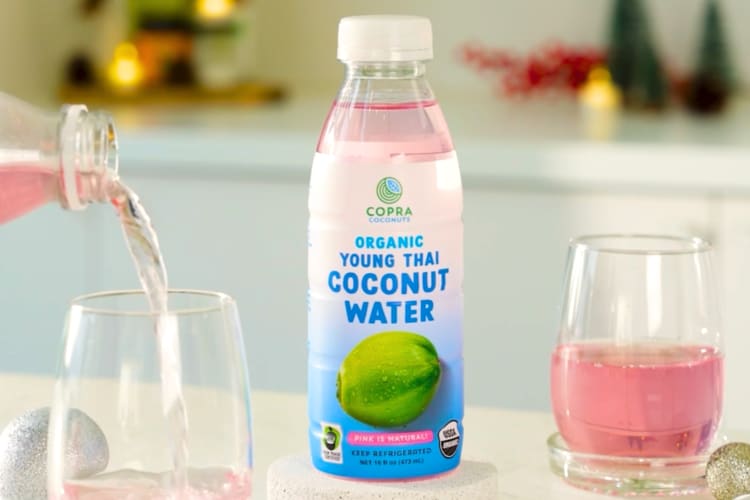 A bottle of coconut water next to a glass with pink coconut water