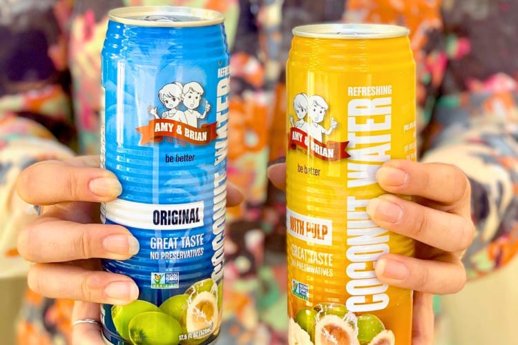 A person holding a blue and a yellow can of coconut water