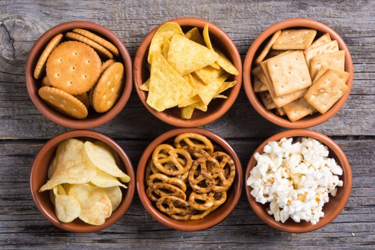 Six different snacks in bowls on a wooden surface