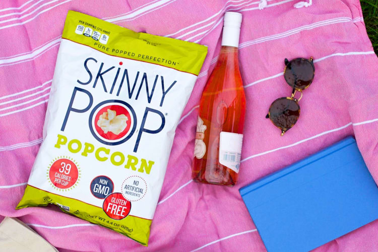 A bag of Skinny Pop on a picnic blanket next to a bottle of wine