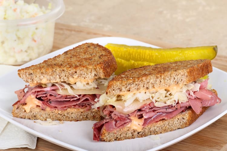 A Reuben sandwich served with a pickle on the side.