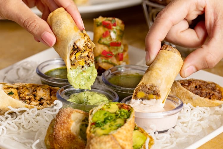 People dipping egg rolls from a platter into sauces