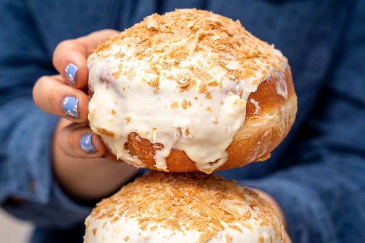 A person holding filled donuts topped with frosting