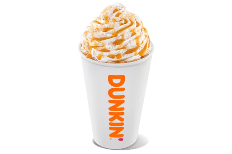 A white Dunkin' cup with coffee topped with whipped cream and caramel