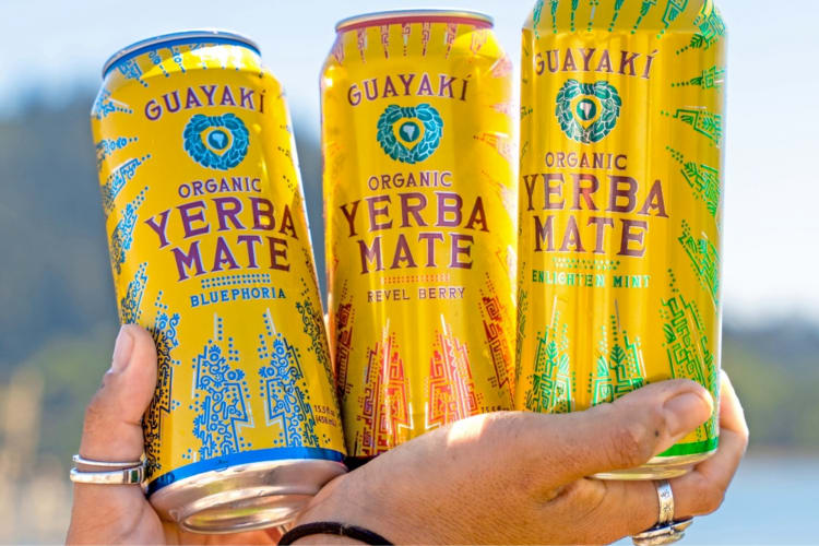 A person holding three cans of Guayaki yerba mate