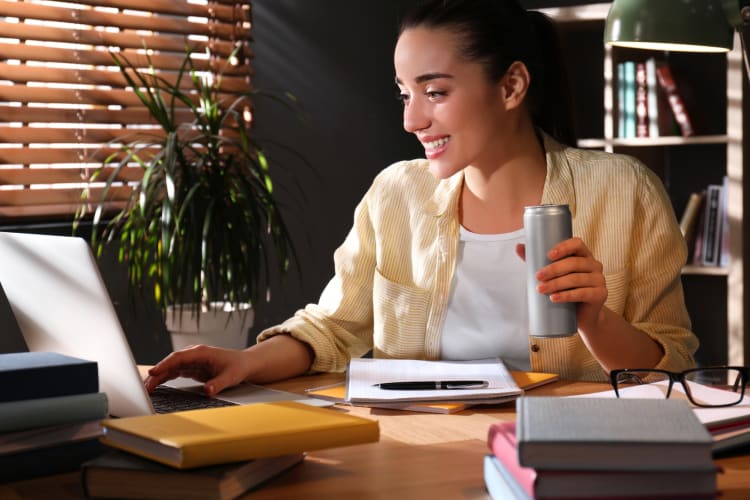 A person working at a desk, holding an energy drink
