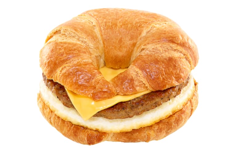 A croissant with eggs, cheese and a sausage patty