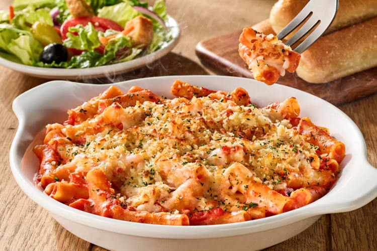 A bowl of ziti al forno next to salad and breadsticks