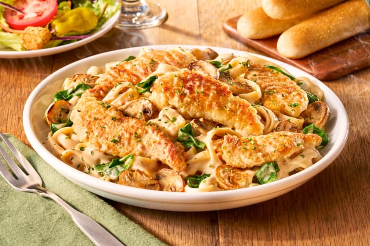 A plate of chicken Marsala fettuccine next to breadsticks and salad