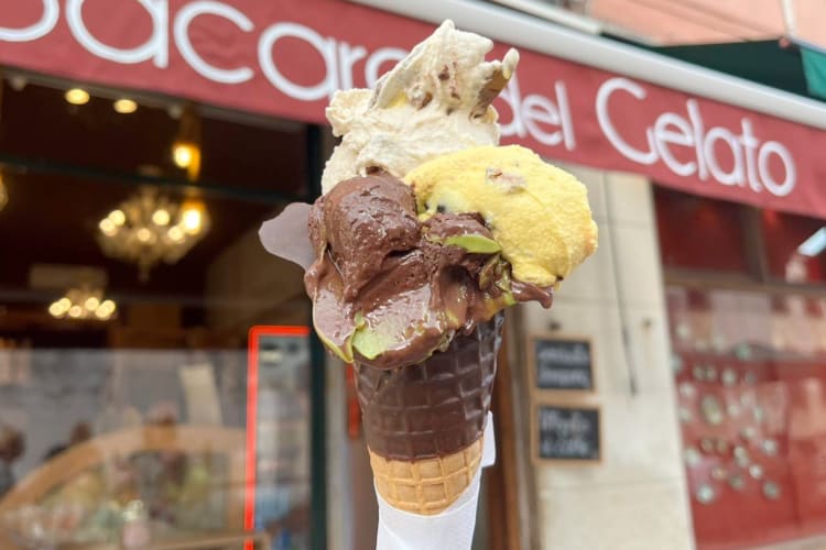 A person holding a chocolate-dipped cone with different types of gelato