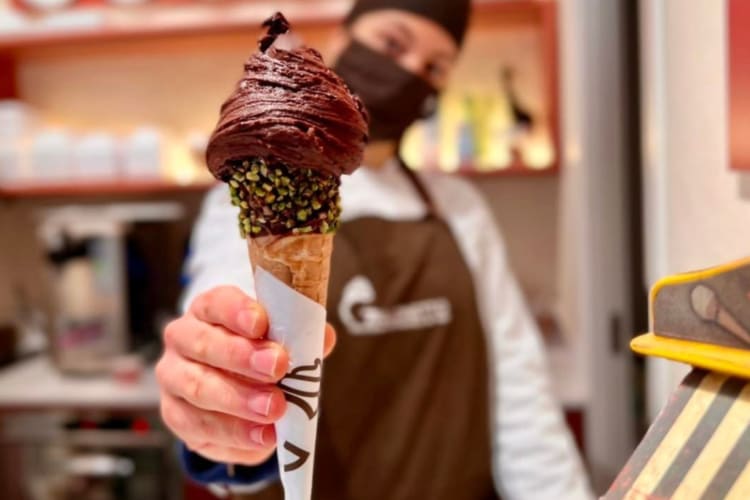 A person handing over an ice cream cone filled with gelato