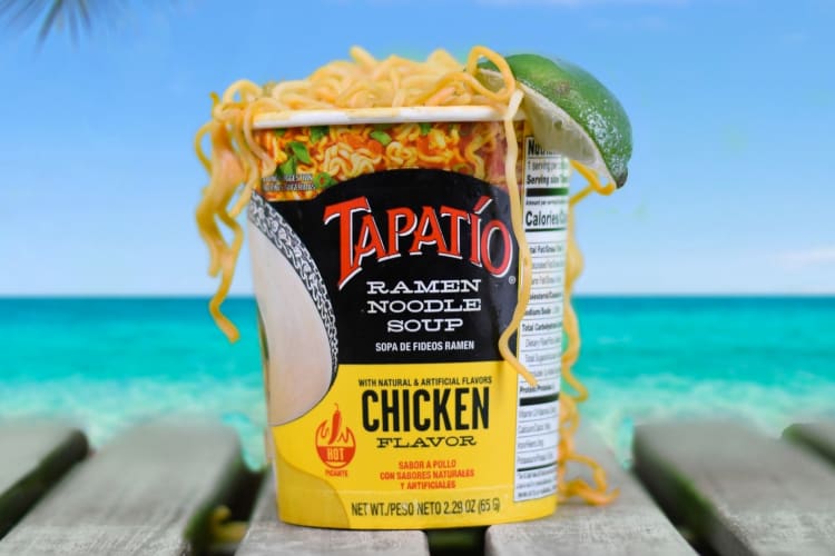 A cup of instant noodles with a slice of lime next to the ocean