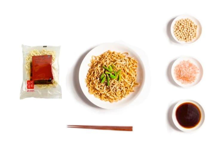A pack of noodles next to a plate of noodles and seasonings