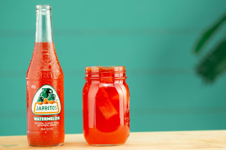 A watermelon Jarritos next to a glass of the soda