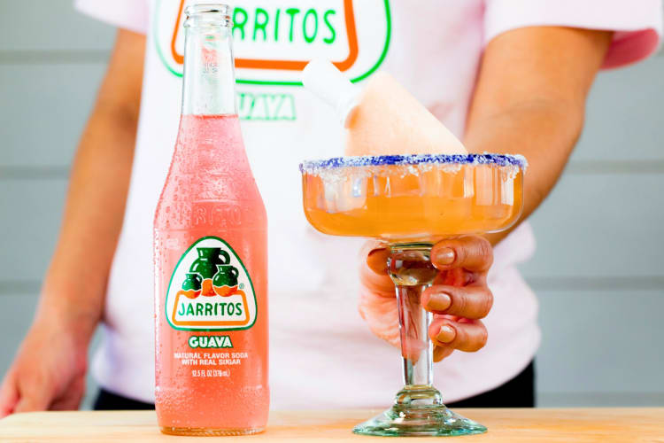 A guava-flavored Jarrito soda next to pink soda in a glass