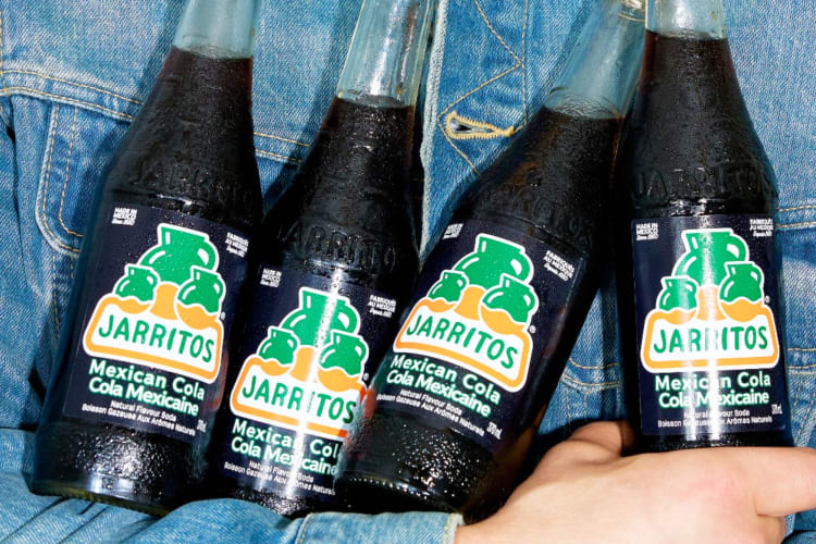 A person in a denim jacket holding Mexican Cola Jarritos