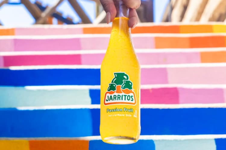 A person holding a passion fruit flavor of Jarritos