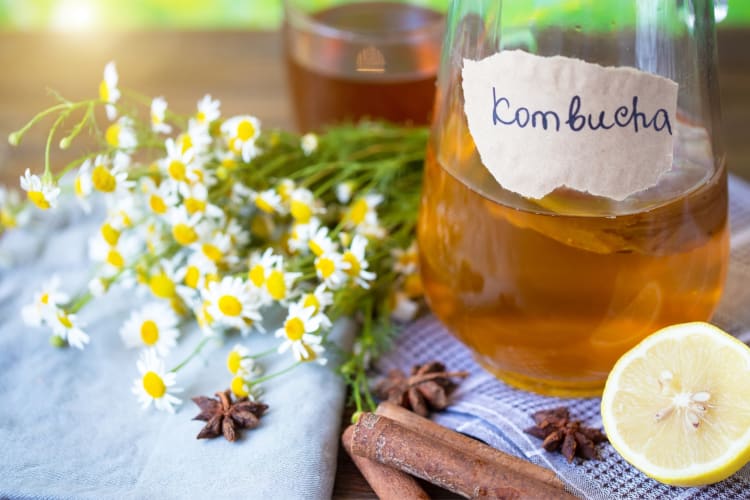 A jug of kombucha next to cinnamon, lemon and fresh flowers