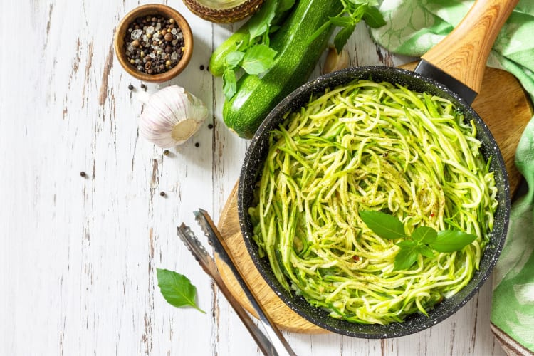 A pan of zucchini noodles next to other ingredients