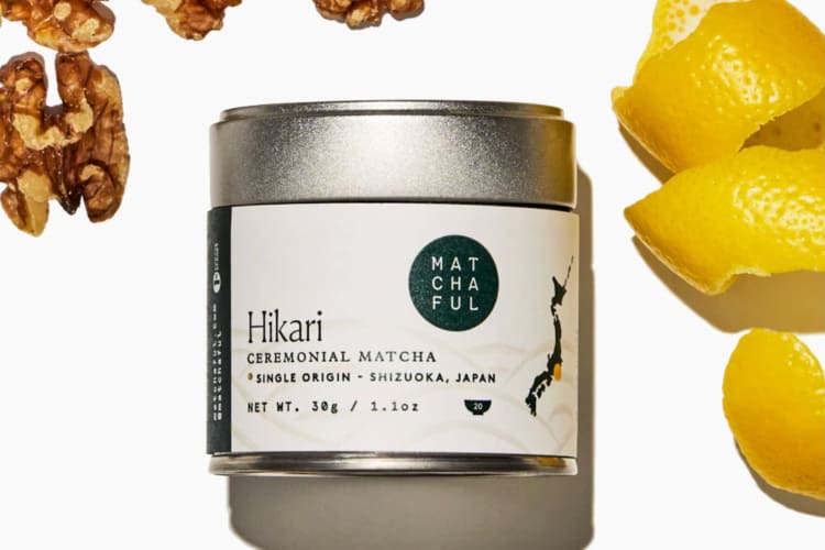 A tin of matcha next to lemon peel and walnuts
