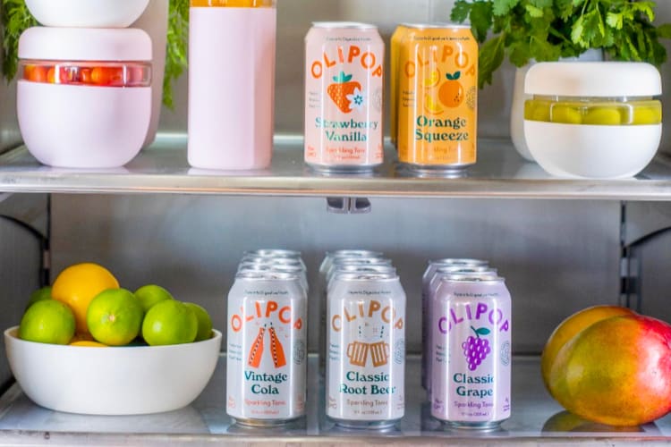 Cans of Olipop soda and fresh produce in a fridge