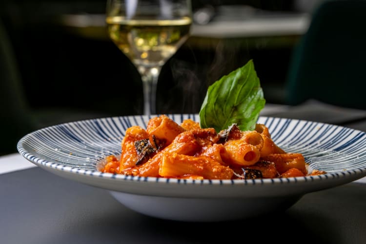A bowl of pasta with tomato sauce next to a glass of wine