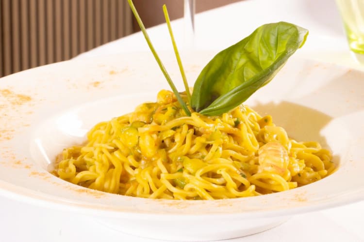 A plate of pasta with a yellow sauce and basil