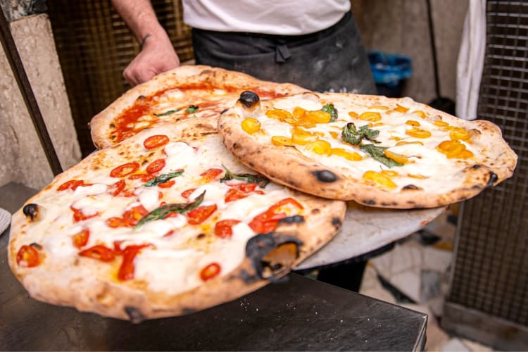 A person holding a pizza peel with three different pizzas