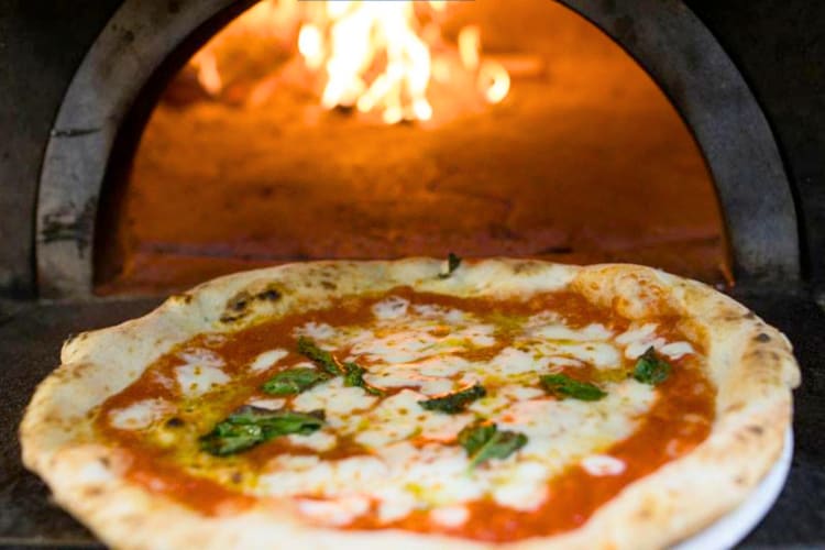 A Margherita pizza being taken out of a pizza oven