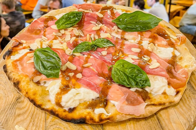 A pizza with prosciutto, stracciata and basil