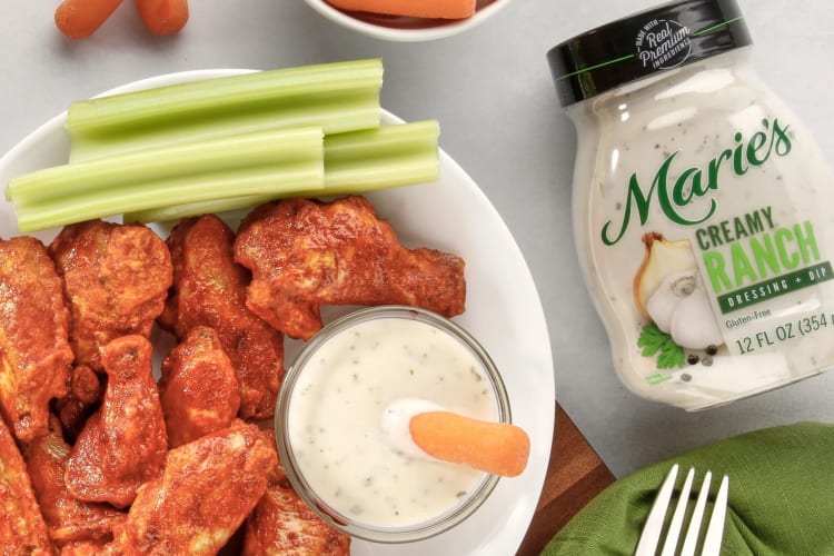 A jar of ranch dressing next to chicken wings and vegetable sticks