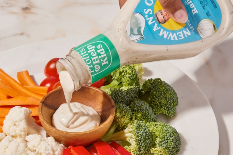 A person pouring ranch into a bowl on a vegetable platter