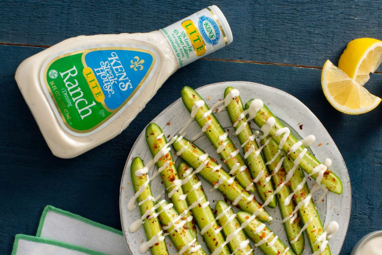 A bottle of ranch next to a plate of pickle spears drizzled with ranch