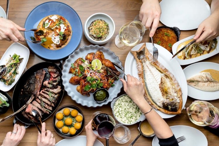 A selection of dishes on a table with diners helping themselves