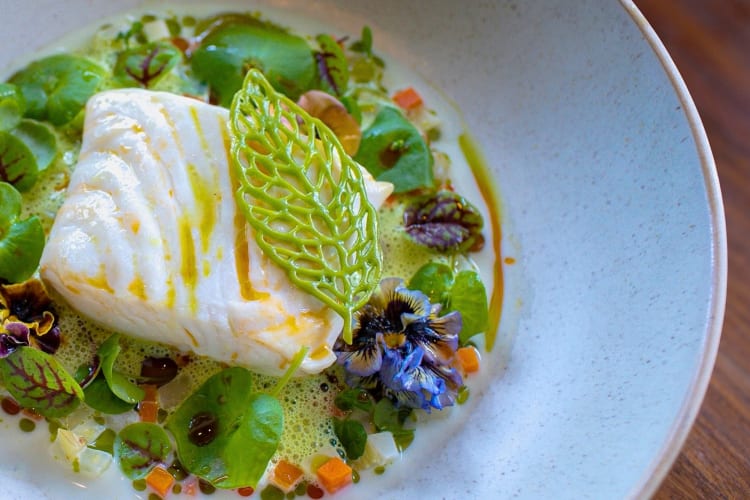 An elegant fish dish with vegetables and edible flowers