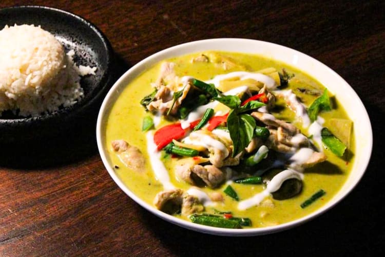 A plate of Thai green curry and a bowl of rice on a table