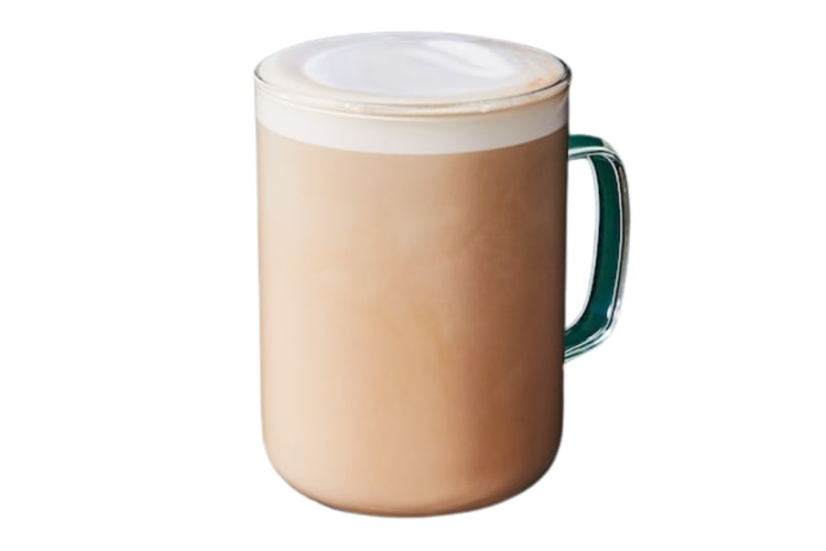 A hot chai latte topped with foam in a glass mug