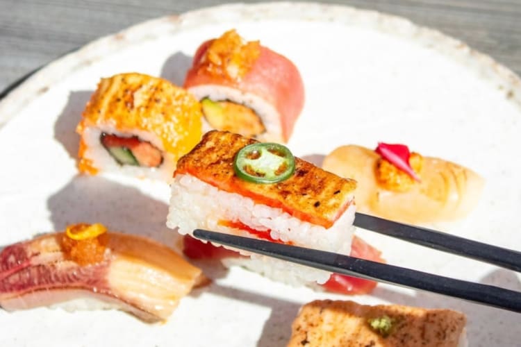 A person using chopsticks to pick up oshi from a plate of sushi
