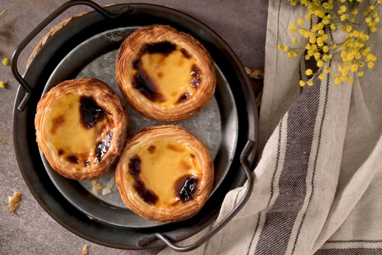 Portuguese custard tarts in a dish next to a cloth