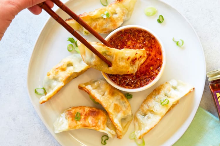 A person dipping a gyoza into chile sauce