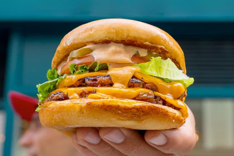 A person holding a veggie burger with salad, cheese and sauce